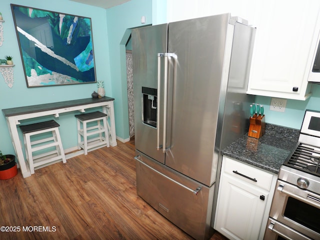 kitchen featuring dark wood-style floors, white cabinetry, stainless steel appliances, and dark stone counters