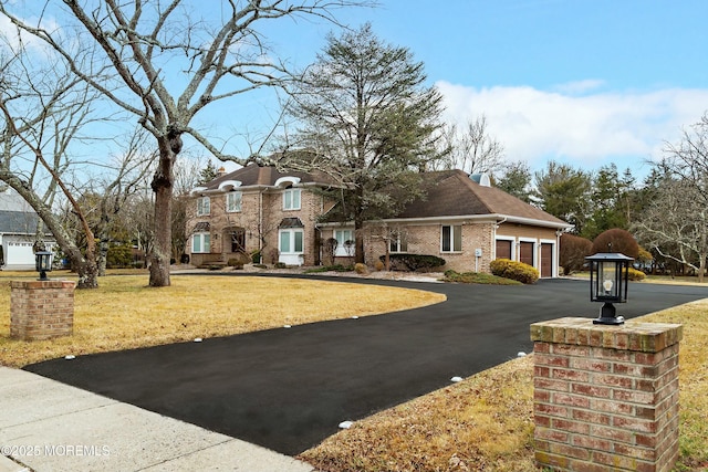 view of front of house with a garage, brick siding, driveway, a front lawn, and a chimney