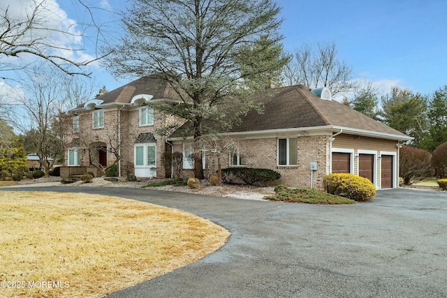 traditional-style house featuring driveway, brick siding, a chimney, and an attached garage