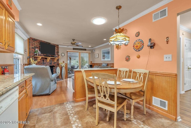 dining room with visible vents, wainscoting, a brick fireplace, and ornamental molding