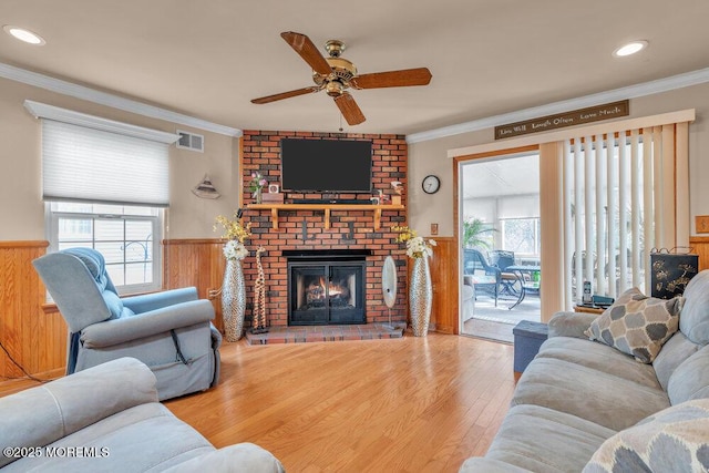 living room featuring visible vents, a brick fireplace, crown molding, wainscoting, and wood finished floors