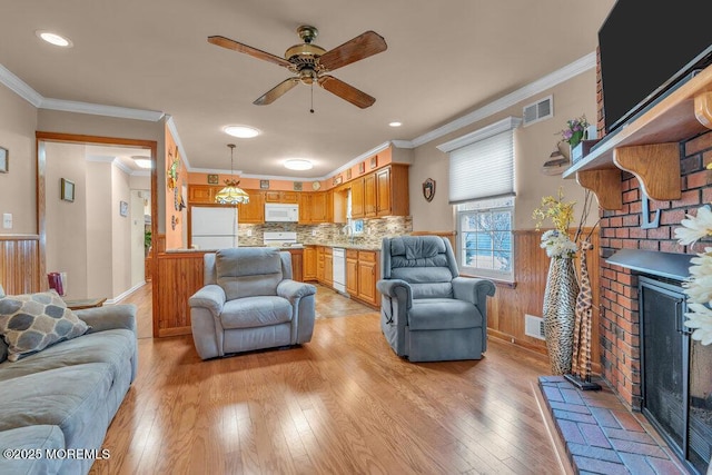 living area with visible vents, light wood-style floors, a brick fireplace, and wainscoting