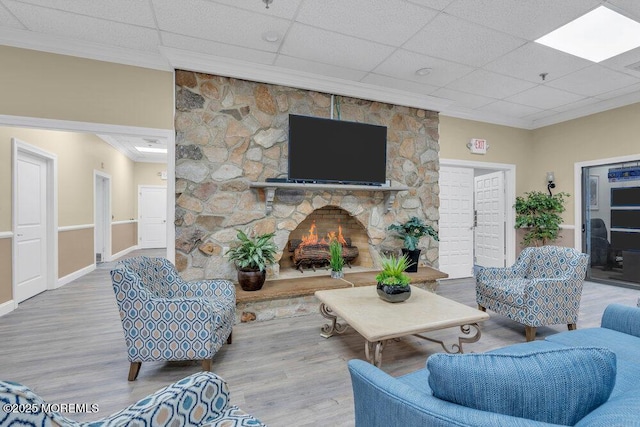 living room featuring a paneled ceiling, a stone fireplace, wood finished floors, and crown molding