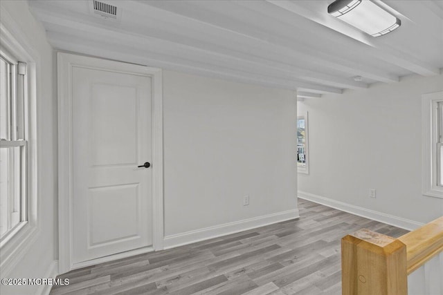 unfurnished room with light wood-style floors, visible vents, baseboards, and beamed ceiling