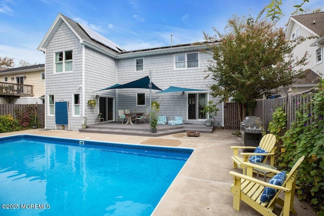 rear view of property featuring a fenced in pool, solar panels, an outdoor fire pit, a patio area, and a fenced backyard