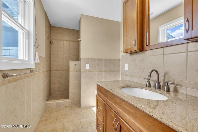 full bathroom with tiled shower, vanity, and tile walls