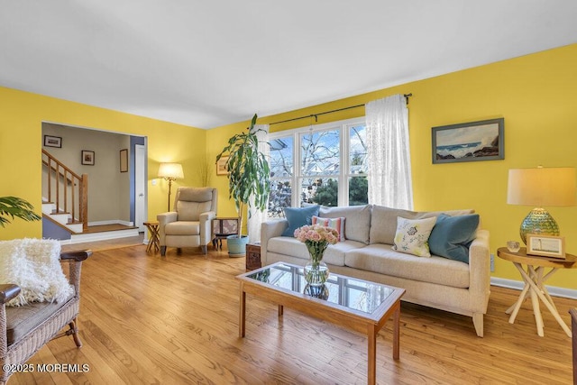 living room featuring stairway, light wood-style flooring, and baseboards