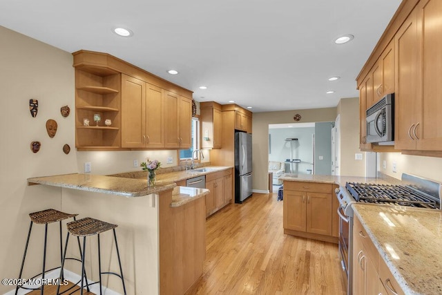 kitchen with appliances with stainless steel finishes, a peninsula, light wood-type flooring, open shelves, and a sink