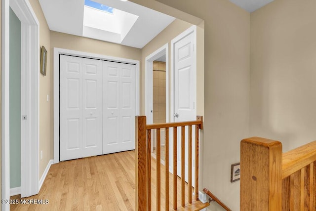 hall with a skylight, baseboards, light wood finished floors, and an upstairs landing