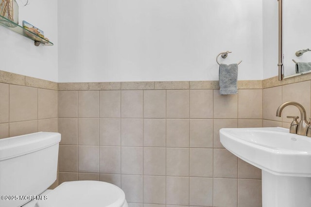 bathroom with a sink, tile walls, and toilet