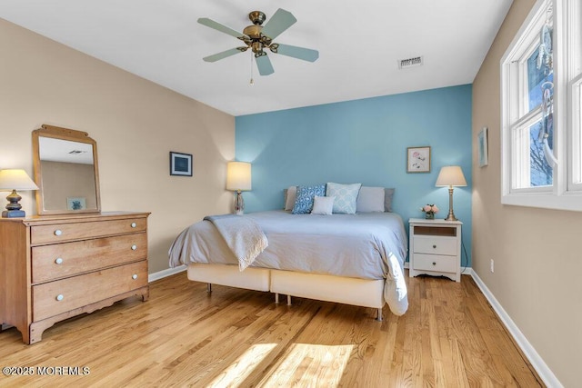 bedroom featuring a ceiling fan, light wood-style flooring, visible vents, and baseboards