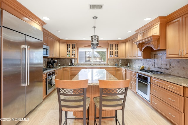 kitchen featuring visible vents, a kitchen island, glass insert cabinets, light stone countertops, and stainless steel appliances