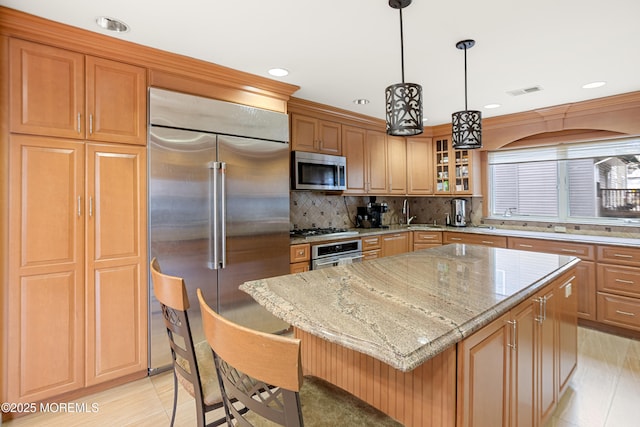 kitchen featuring light stone counters, stainless steel appliances, a breakfast bar, a kitchen island, and glass insert cabinets