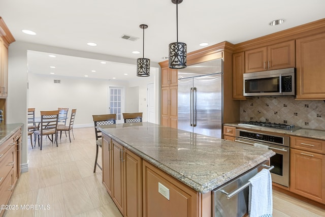 kitchen featuring visible vents, decorative backsplash, a kitchen island, appliances with stainless steel finishes, and light stone countertops