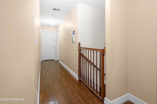 corridor with dark wood-type flooring, an upstairs landing, visible vents, and baseboards