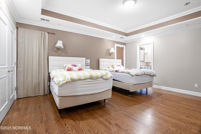 bedroom featuring a tray ceiling, wood finished floors, visible vents, and crown molding