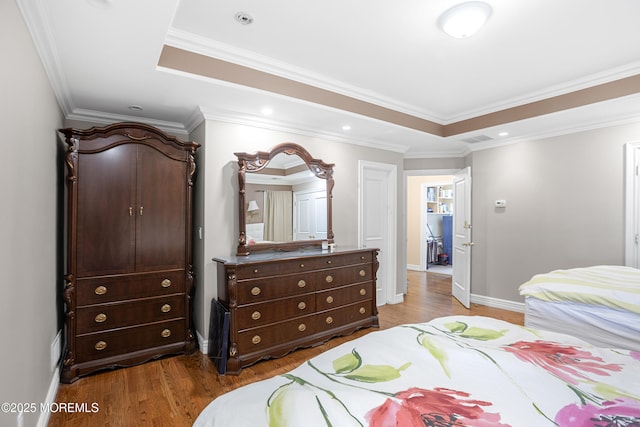 bedroom with baseboards, visible vents, ornamental molding, wood finished floors, and a tray ceiling