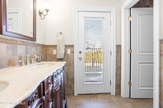 bathroom featuring tile walls, double vanity, wainscoting, a sink, and tile patterned flooring