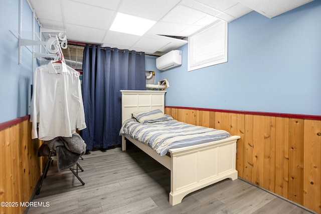 bedroom featuring a wall unit AC, wooden walls, a paneled ceiling, and wainscoting