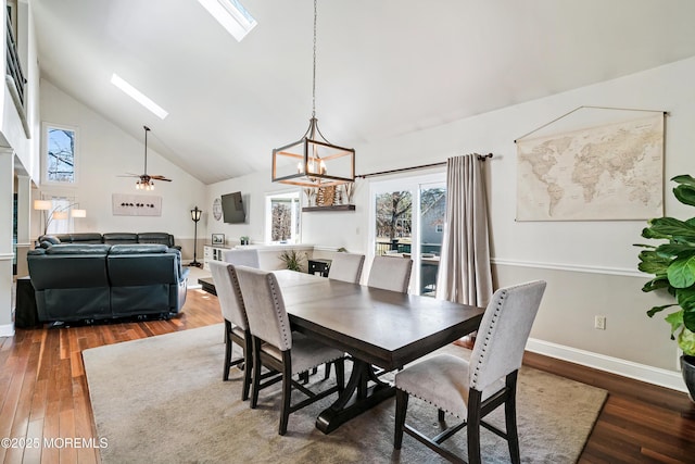 dining space with high vaulted ceiling, hardwood / wood-style flooring, ceiling fan with notable chandelier, a skylight, and baseboards