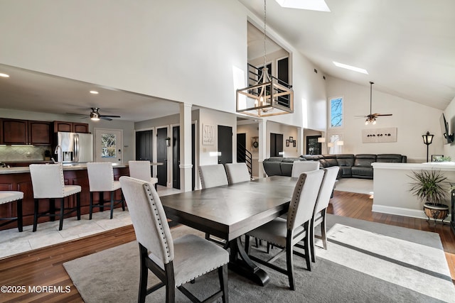 dining room with light wood-type flooring, a skylight, and ceiling fan with notable chandelier