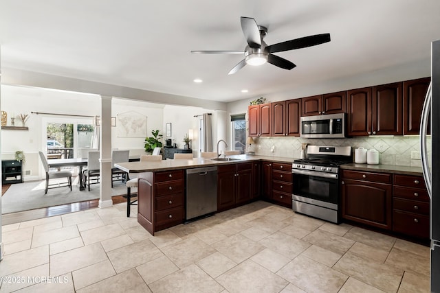 kitchen with a breakfast bar area, stainless steel appliances, a peninsula, a sink, and backsplash