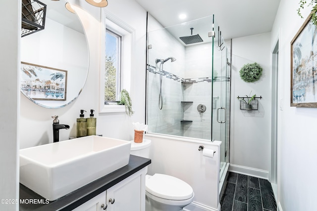 bathroom with a stall shower, baseboards, toilet, vanity, and wood finish floors