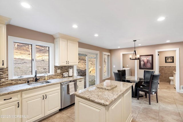 kitchen with light stone counters, a sink, a center island, dishwasher, and pendant lighting