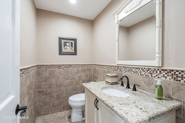 half bath with a wainscoted wall, vanity, toilet, and tile walls