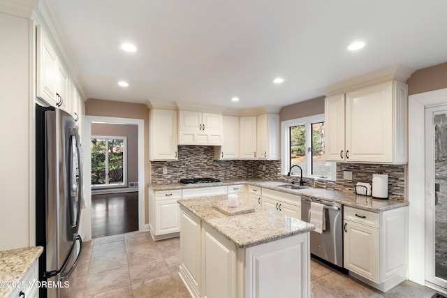 kitchen with stainless steel appliances, light stone countertops, a sink, and tasteful backsplash