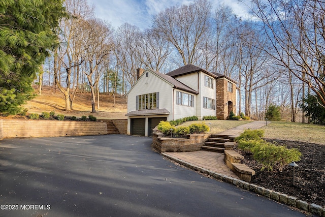 view of front of home featuring aphalt driveway, a chimney, and an attached garage