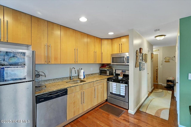 kitchen featuring light stone counters, wood finished floors, a sink, appliances with stainless steel finishes, and light brown cabinetry