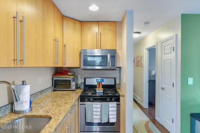 kitchen with a toaster, a baseboard heating unit, a sink, appliances with stainless steel finishes, and light stone countertops