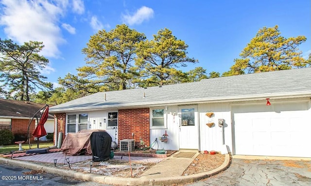 ranch-style house featuring a garage, a shingled roof, central AC unit, and brick siding