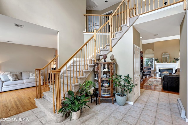 stairs featuring a baseboard heating unit, tile patterned flooring, a towering ceiling, and visible vents