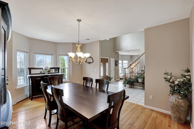 dining space featuring light wood-type flooring, stairway, a baseboard heating unit, and a chandelier