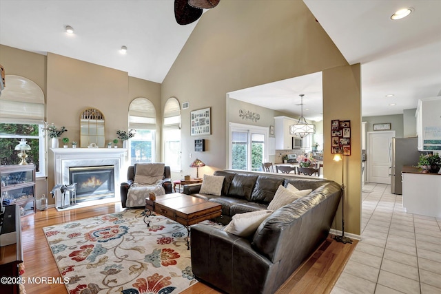 living room with high vaulted ceiling, a glass covered fireplace, light wood finished floors, and recessed lighting