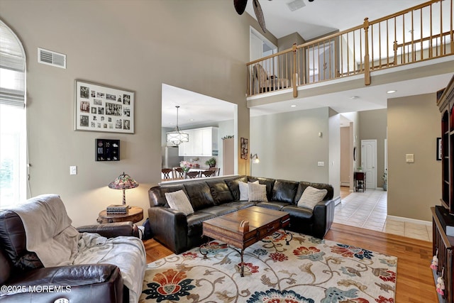 living area with light wood finished floors, a high ceiling, visible vents, and a wealth of natural light