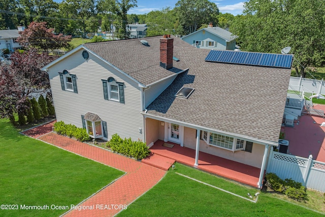 traditional home featuring a shingled roof, a chimney, fence, roof mounted solar panels, and a front yard