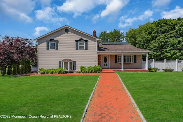 tri-level home with a front yard, covered porch, fence, and solar panels