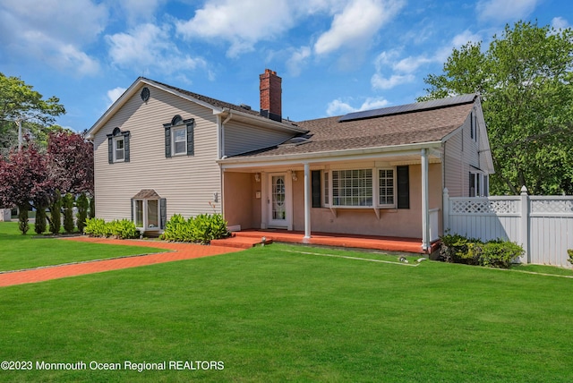 split level home with covered porch, fence, roof mounted solar panels, a front lawn, and a chimney