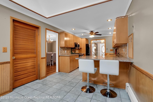 kitchen featuring a wainscoted wall, appliances with stainless steel finishes, a peninsula, baseboard heating, and a sink