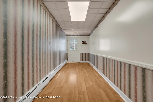 hallway featuring a baseboard radiator, a wainscoted wall, a drop ceiling, and wood finished floors