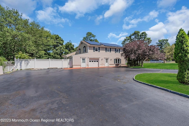 view of front of house featuring a garage, solar panels, fence, driveway, and a front yard