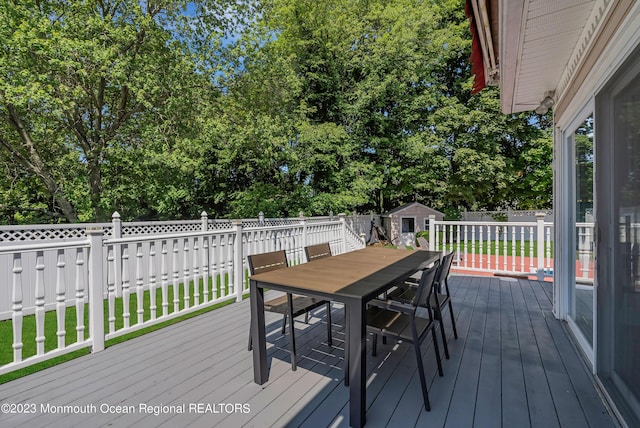 wooden terrace with fence, a storage unit, an outdoor structure, and outdoor dining space