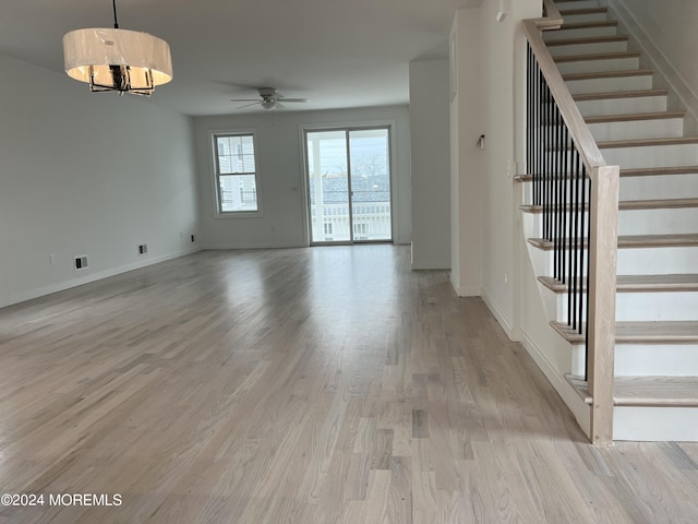 interior space with stairway, ceiling fan with notable chandelier, baseboards, and light wood-style floors