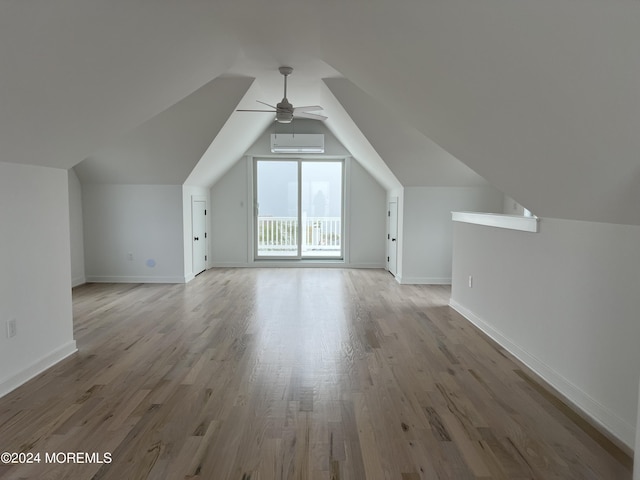 bonus room featuring lofted ceiling, wood finished floors, a wall unit AC, baseboards, and ceiling fan