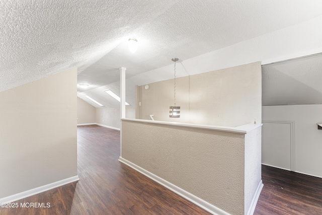 additional living space with lofted ceiling, a textured wall, a textured ceiling, wood finished floors, and baseboards