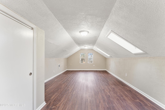 additional living space with vaulted ceiling with skylight, dark wood-style flooring, a textured ceiling, and baseboards