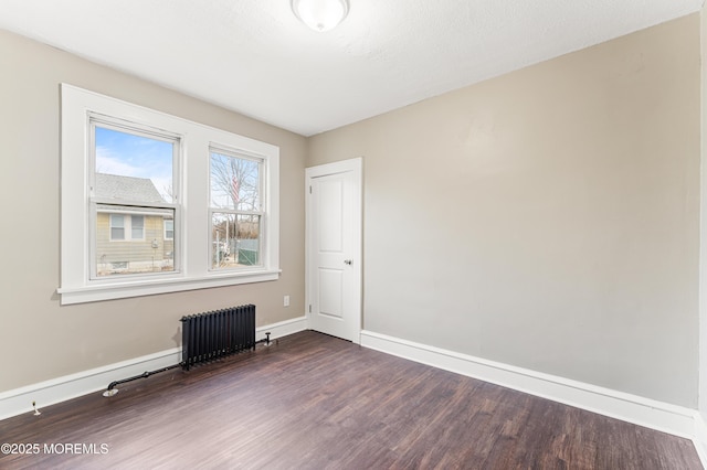 empty room with radiator heating unit, baseboards, and dark wood-style flooring